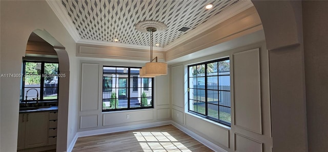 interior space with crown molding, wood finished floors, arched walkways, and a wealth of natural light