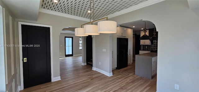 kitchen featuring light wood finished floors, arched walkways, crown molding, and freestanding refrigerator