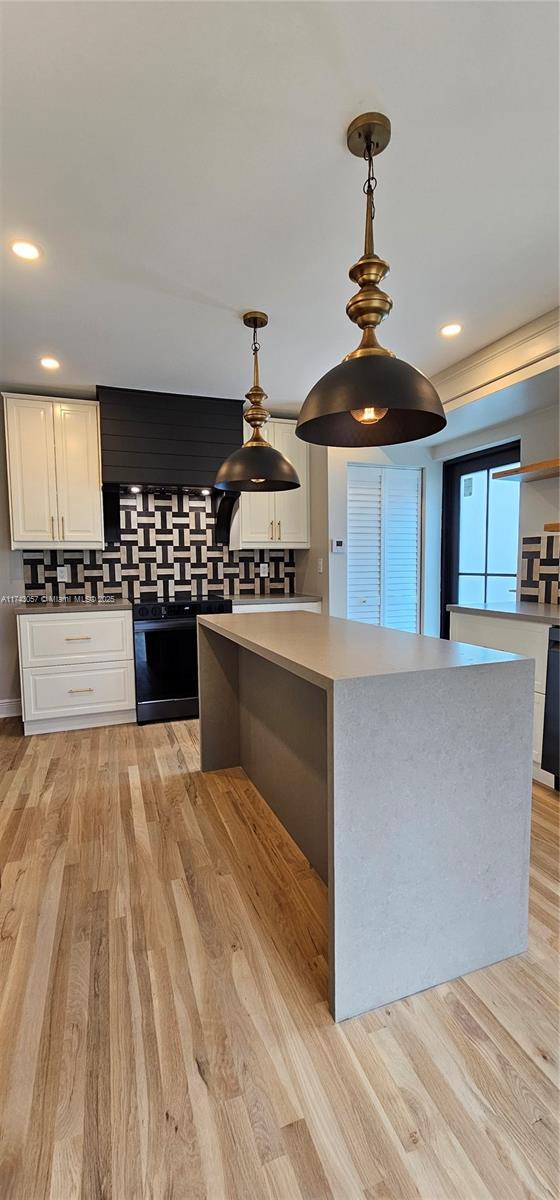 kitchen with decorative light fixtures, light wood-style flooring, white cabinets, and a kitchen island