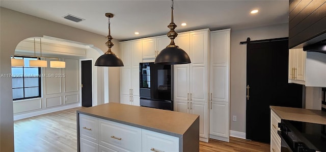 kitchen with black appliances, white cabinets, a barn door, and visible vents