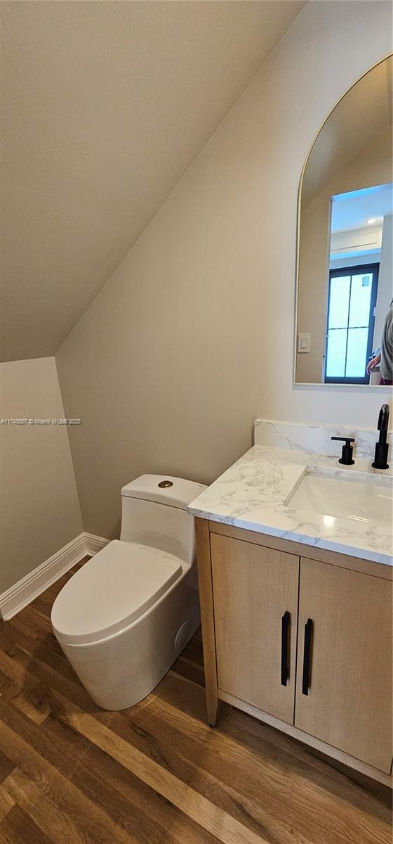 half bathroom with baseboards, toilet, lofted ceiling, wood finished floors, and vanity