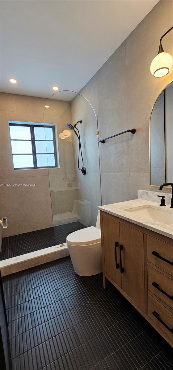 bathroom with tile walls, toilet, tiled shower, and vanity