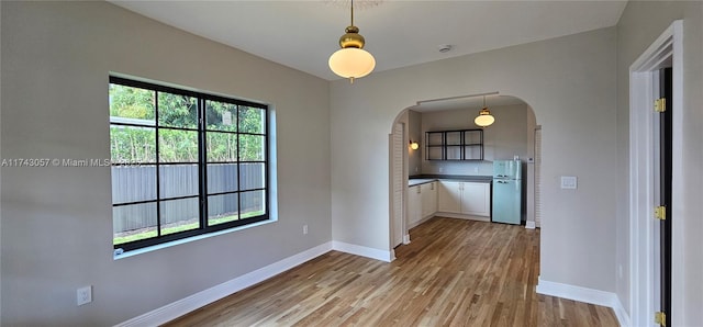 unfurnished dining area featuring baseboards, arched walkways, and light wood-style floors