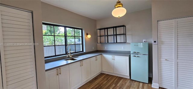 kitchen with wood finished floors, freestanding refrigerator, a sink, white cabinetry, and decorative light fixtures