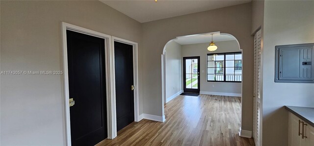 entrance foyer featuring electric panel, baseboards, arched walkways, and wood finished floors