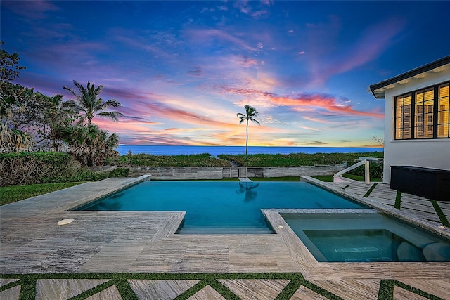 pool at dusk featuring a deck with water view and an in ground hot tub