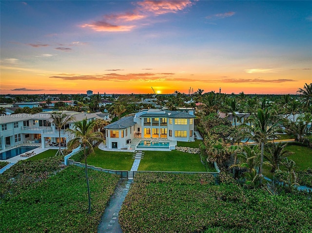 back house at dusk featuring a balcony and a yard