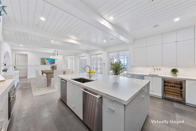 kitchen with wine cooler, sink, hanging light fixtures, an island with sink, and white cabinets