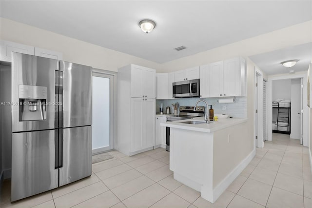 kitchen with appliances with stainless steel finishes, light tile patterned floors, white cabinets, and decorative backsplash