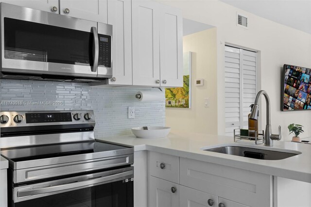 kitchen with sink, backsplash, white cabinets, and appliances with stainless steel finishes