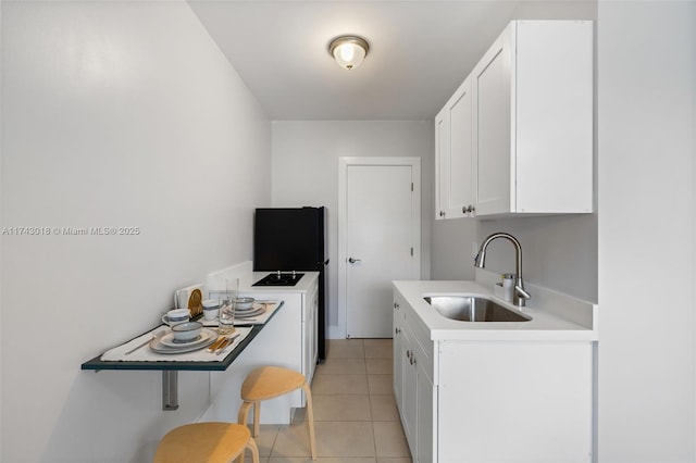 kitchen with sink, light tile patterned floors, white cabinets, and black refrigerator