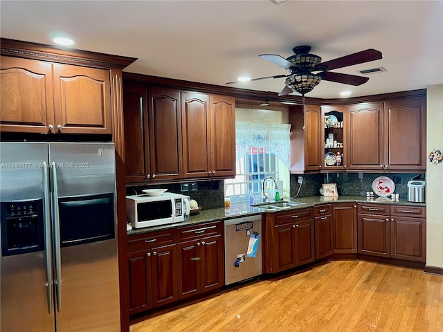kitchen featuring sink, dark stone countertops, stainless steel appliances, decorative backsplash, and light wood-type flooring