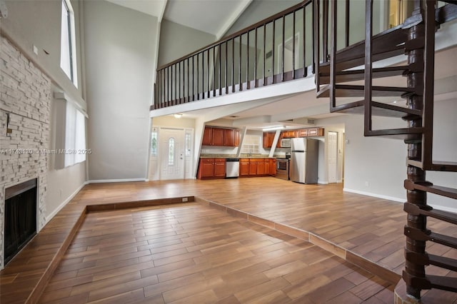 unfurnished living room featuring hardwood / wood-style flooring, a stone fireplace, and a high ceiling