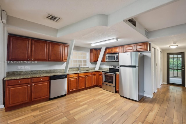 kitchen featuring stainless steel appliances, light stone countertops, sink, and light wood-type flooring