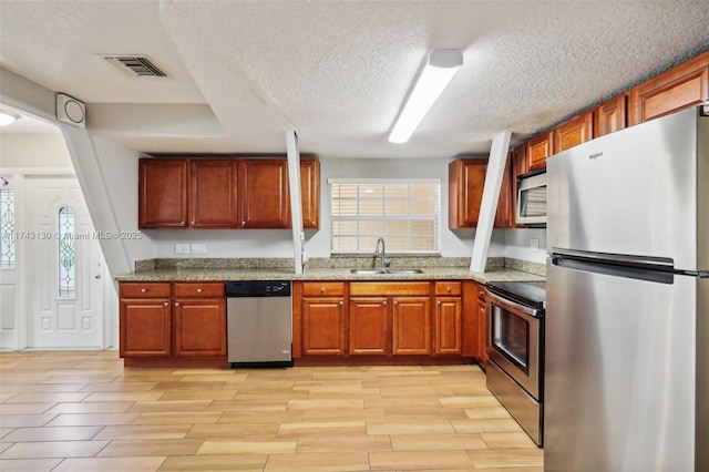 kitchen with appliances with stainless steel finishes, sink, a textured ceiling, and light stone counters