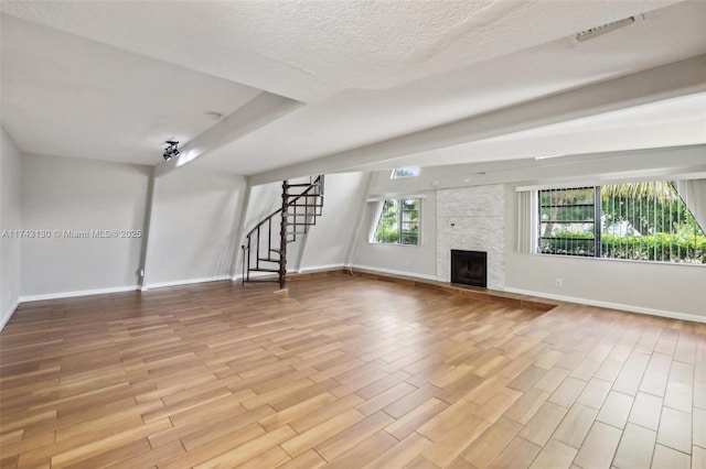 unfurnished living room featuring a stone fireplace, light hardwood / wood-style flooring, and a textured ceiling