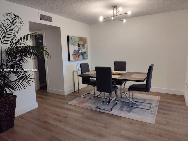 dining room featuring a chandelier, visible vents, a textured ceiling, and wood finished floors