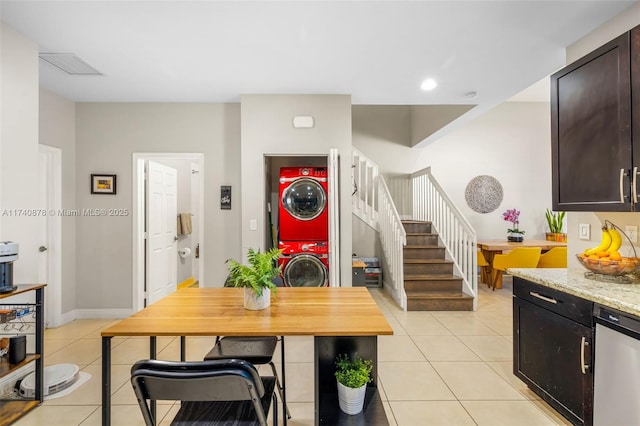 kitchen featuring stacked washer and dryer, dark brown cabinets, stainless steel dishwasher, and light tile patterned flooring