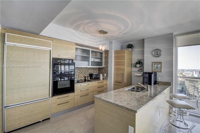 kitchen with tasteful backsplash, sink, hanging light fixtures, black double oven, and light stone counters