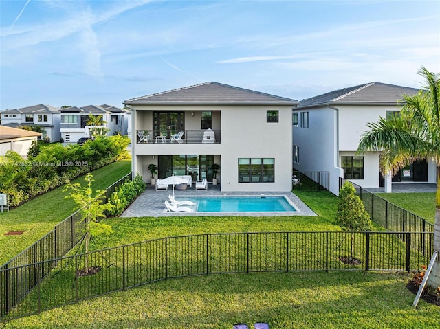 rear view of house featuring a balcony, a fenced in pool, a patio, and a lawn