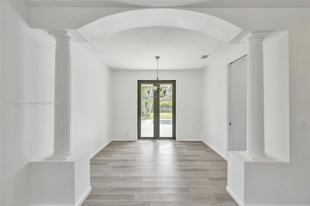 interior space with french doors, light hardwood / wood-style floors, decorative columns, and a textured ceiling