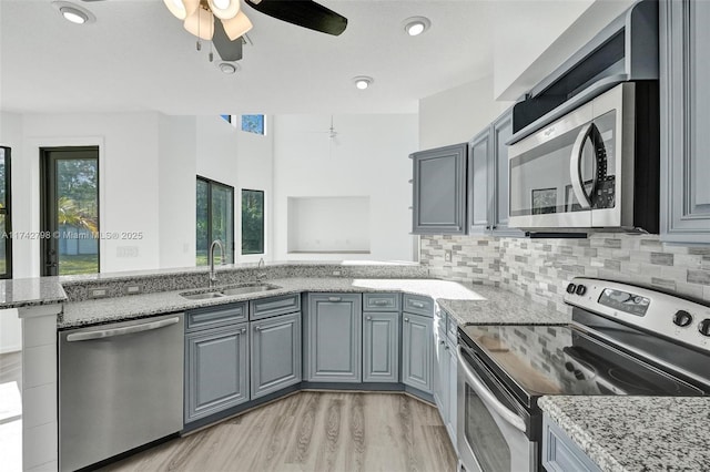 kitchen with sink, gray cabinetry, kitchen peninsula, stainless steel appliances, and light stone countertops