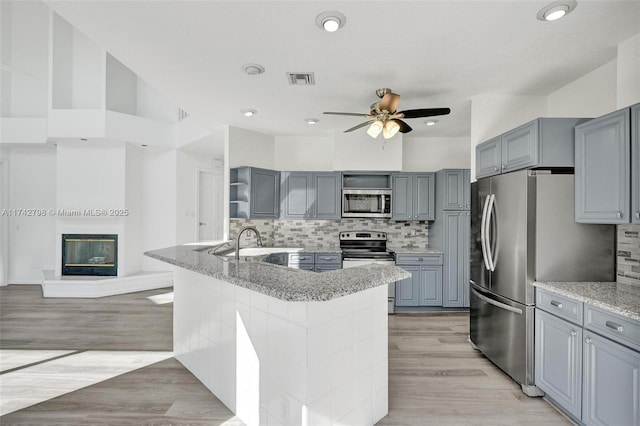 kitchen featuring tasteful backsplash, light hardwood / wood-style flooring, appliances with stainless steel finishes, gray cabinets, and ceiling fan