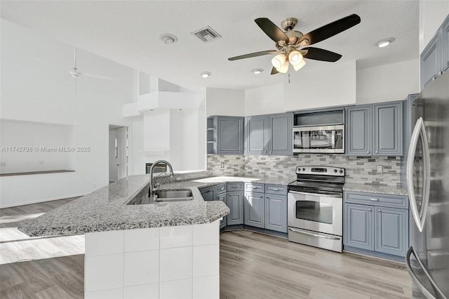 kitchen with sink, appliances with stainless steel finishes, gray cabinetry, light hardwood / wood-style floors, and kitchen peninsula