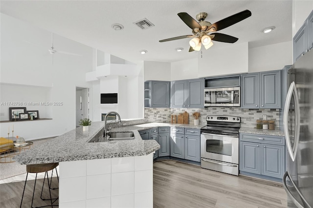 kitchen with a breakfast bar, sink, gray cabinetry, kitchen peninsula, and stainless steel appliances