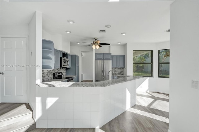 kitchen with gray cabinetry, tasteful backsplash, light wood-type flooring, appliances with stainless steel finishes, and kitchen peninsula