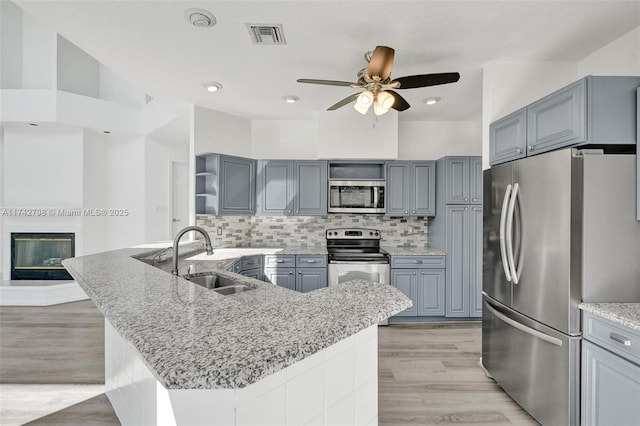 kitchen featuring sink, light hardwood / wood-style flooring, an island with sink, stainless steel appliances, and backsplash