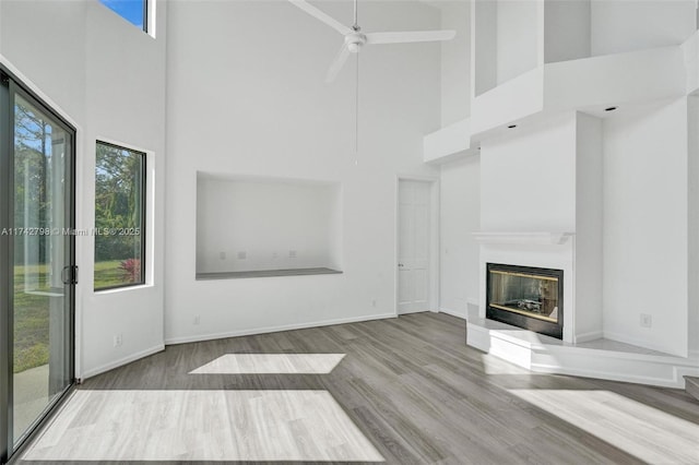 unfurnished living room with a high ceiling, ceiling fan, a healthy amount of sunlight, and light hardwood / wood-style floors