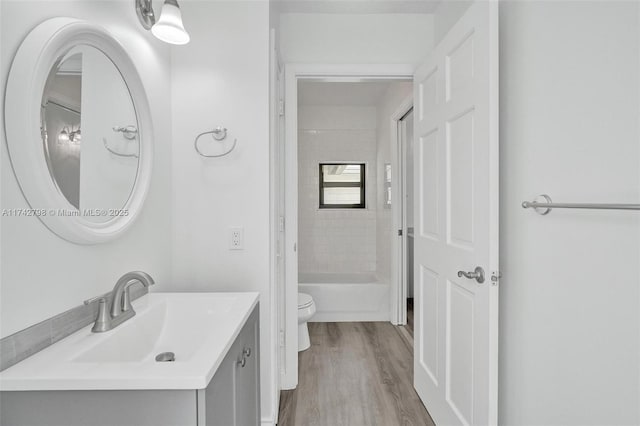 full bathroom with tiled shower / bath combo, vanity, hardwood / wood-style floors, and toilet