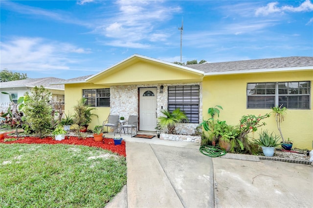 single story home with a front lawn, roof with shingles, and stucco siding