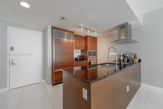 kitchen with light tile patterned flooring, island range hood, sink, built in appliances, and kitchen peninsula