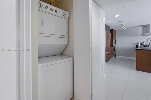 clothes washing area featuring light tile patterned flooring, stacked washer and clothes dryer, and sink