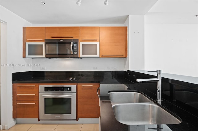 kitchen with dark stone countertops, light tile patterned floors, sink, black cooktop, and stainless steel oven