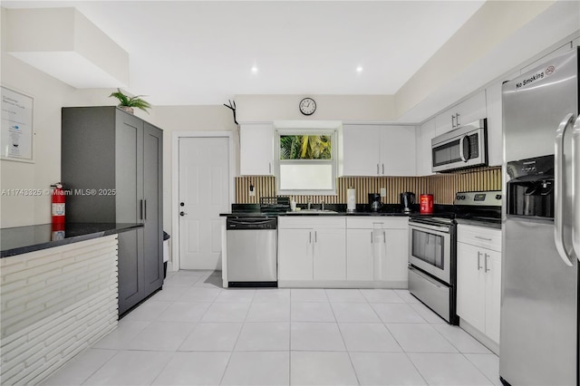 kitchen featuring stainless steel appliances, dark countertops, white cabinetry, and light tile patterned flooring