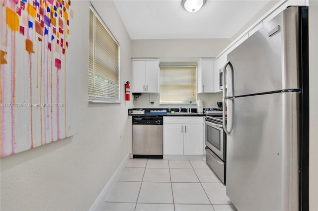 kitchen featuring light tile patterned floors, stainless steel appliances, baseboards, white cabinets, and dark countertops