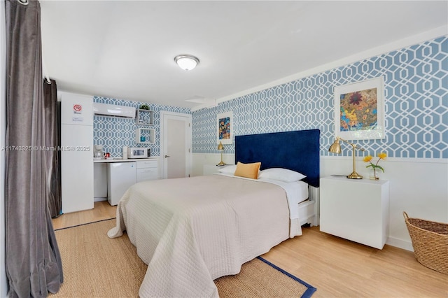 bedroom with an accent wall, light wood-style flooring, and wallpapered walls