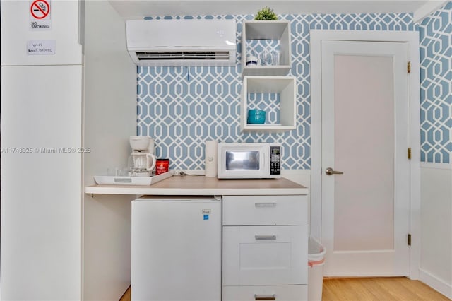 kitchen featuring refrigerator, light countertops, white microwave, a wall mounted air conditioner, and wallpapered walls