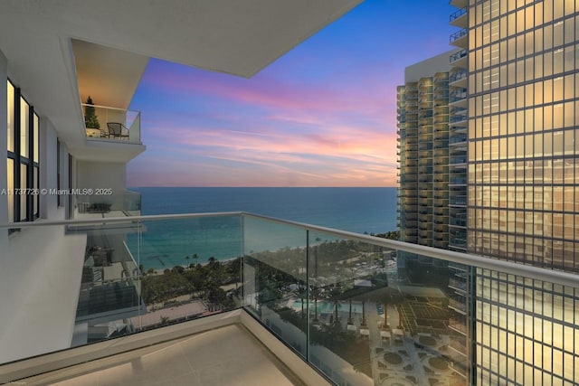 balcony at dusk featuring a water view