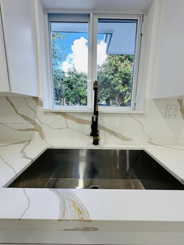 interior details with light stone counters, sink, tasteful backsplash, and white cabinets