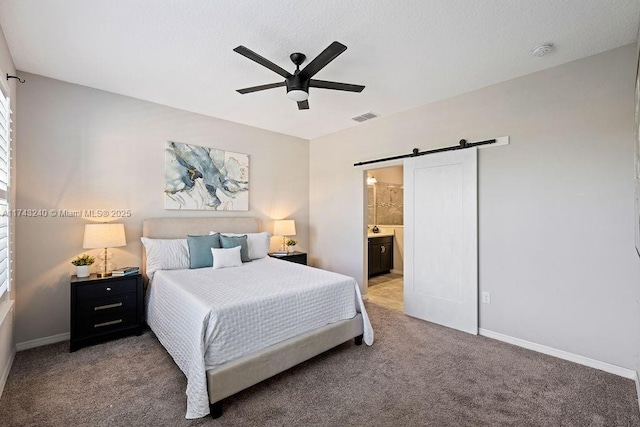 bedroom featuring ceiling fan, connected bathroom, a barn door, and carpet floors