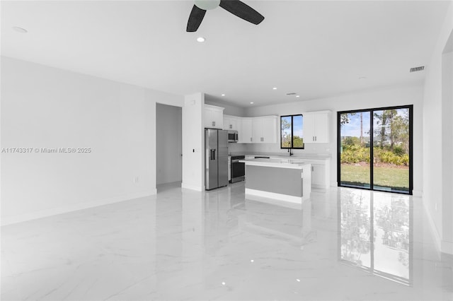 kitchen featuring ceiling fan, appliances with stainless steel finishes, a kitchen island, and white cabinets