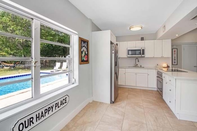 kitchen with light tile patterned floors, stainless steel appliances, a sink, white cabinets, and light countertops