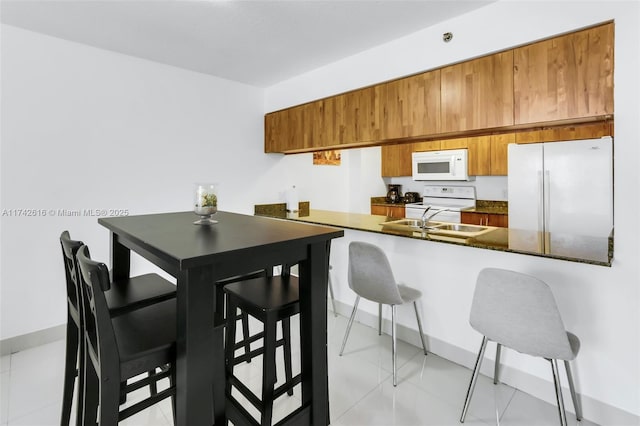 kitchen featuring a breakfast bar, sink, white appliances, and kitchen peninsula