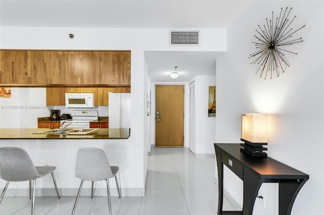 kitchen featuring light tile patterned flooring, white appliances, sink, and a breakfast bar area