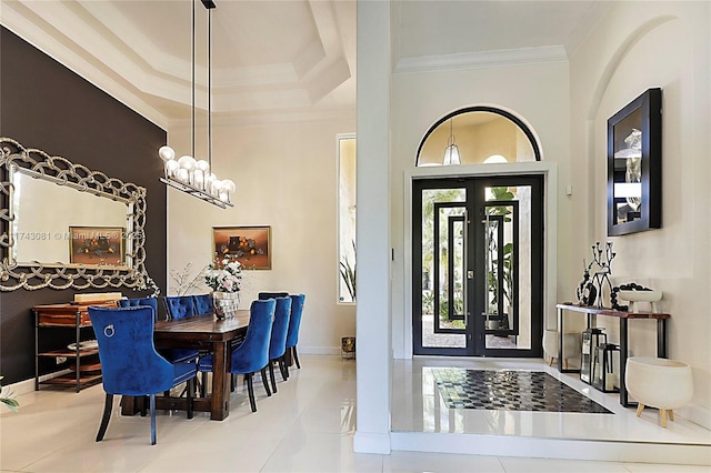 tiled entrance foyer featuring french doors, ornamental molding, a raised ceiling, and a notable chandelier