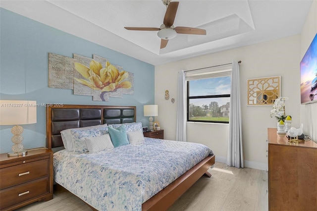 bedroom featuring a tray ceiling, ceiling fan, and light wood-type flooring